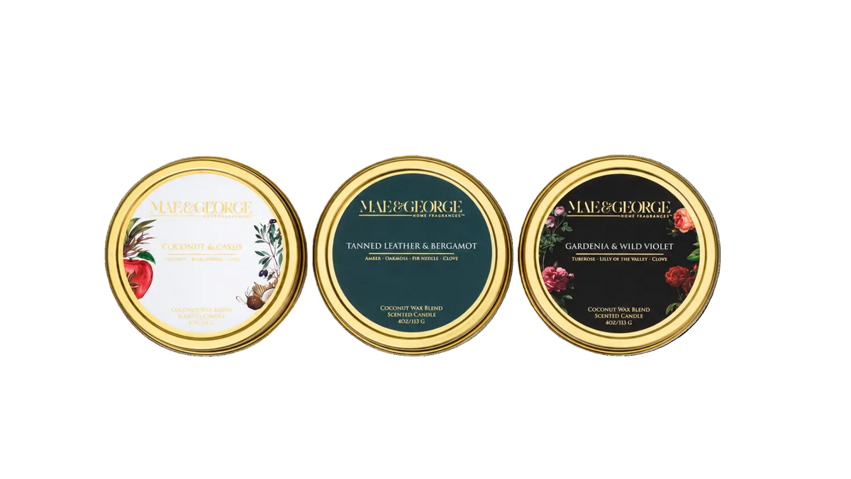 Three round perfume or fragrance bottles with gold caps arranged side by side on a light gray background. The labels are cream, dark green, and dark green with gold lettering and botanical/floral illustrations.