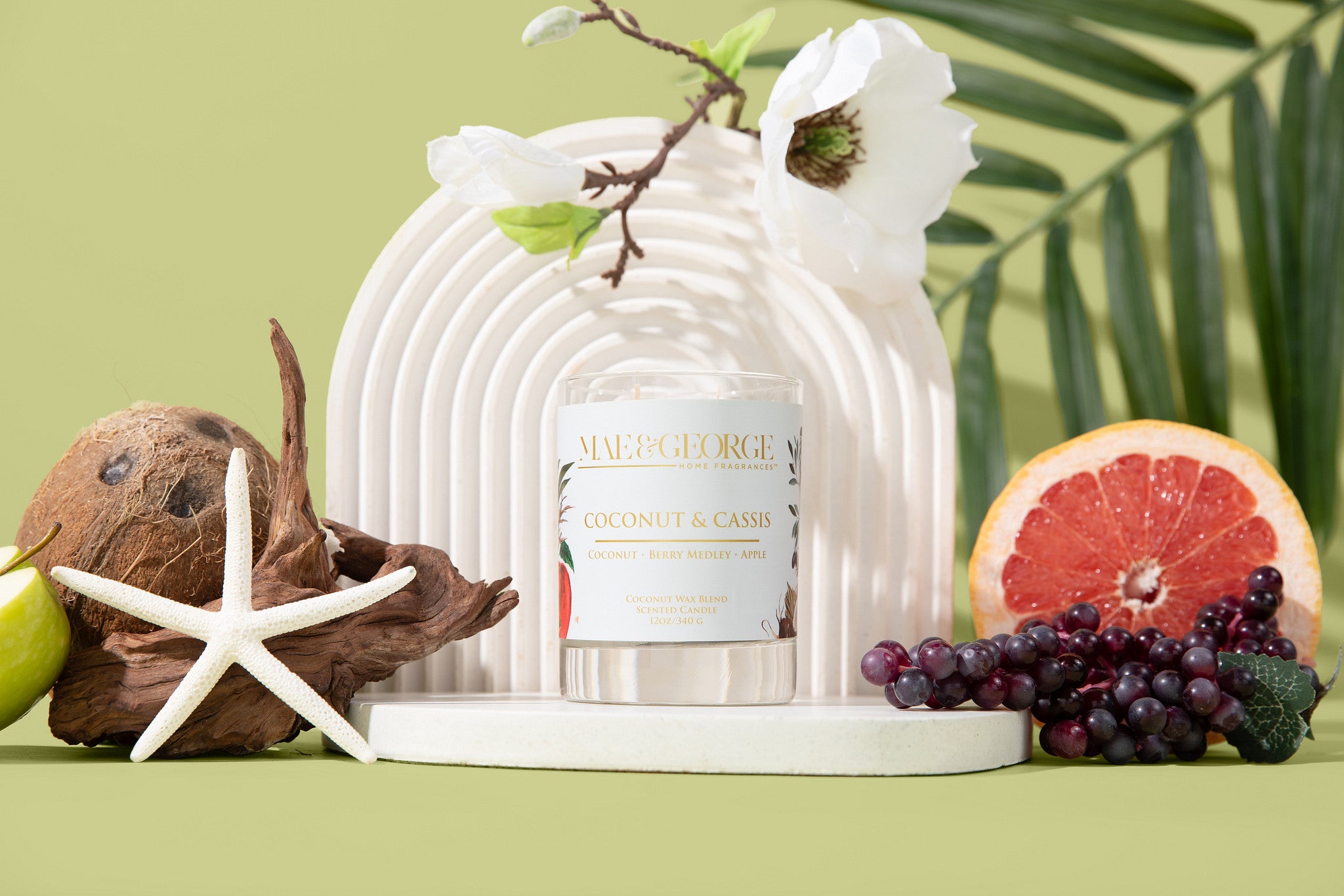 Candle with coconut and grapefruit notes on a decorative stand with fruits and leaves.